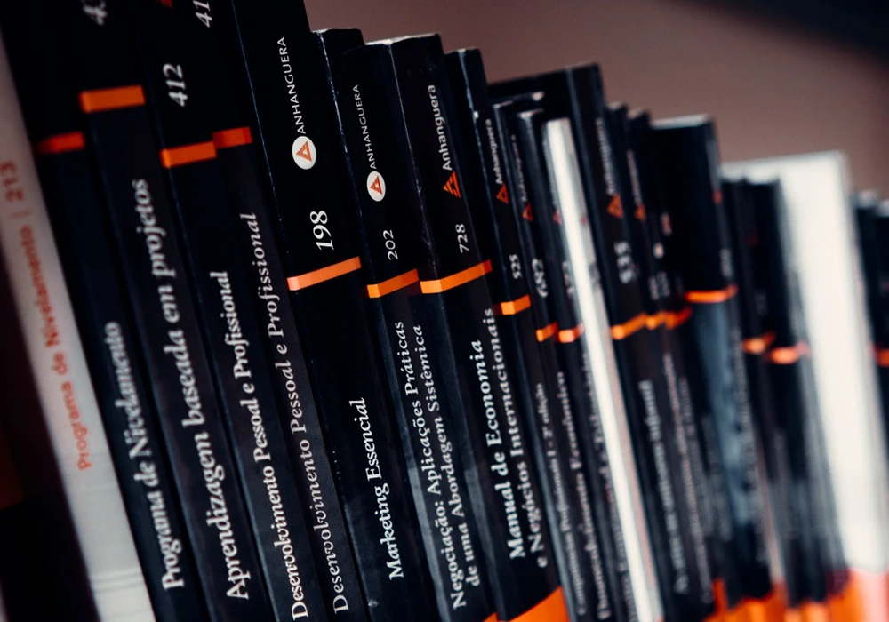 Coleção de livros da Anhanguera em estante com títulos de áreas acadêmicas e profissionais.