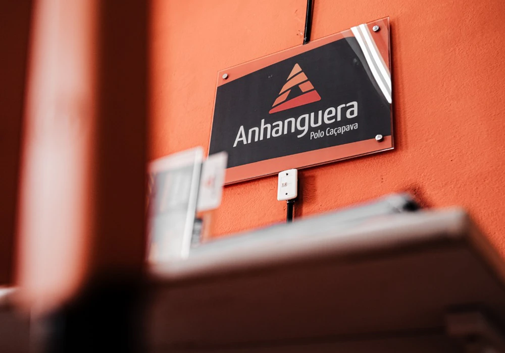 Logotipo do Polo Anhanguera Caçapava fixado em parede laranja interna.